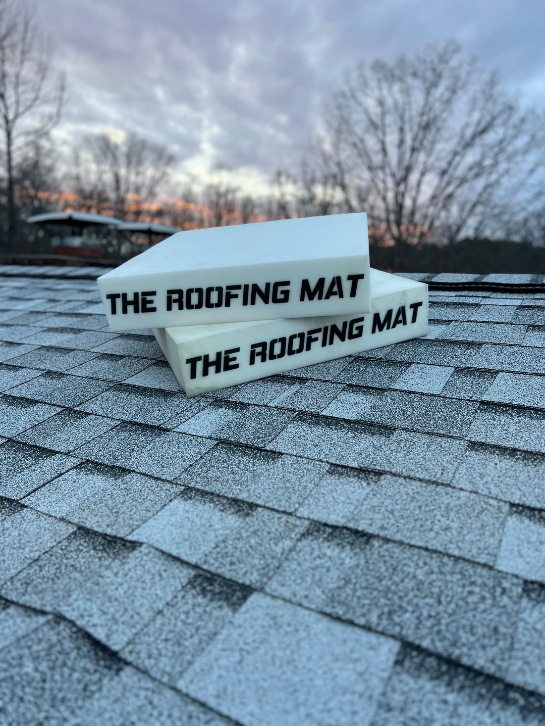 The Roofing Mat stacked on asphalt shingles during sunset, showcasing its reflective white surface and durable design—engineered for roofer safety, comfort, and heat resistance.
